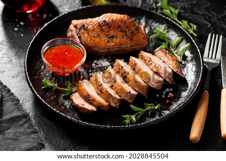 Roasted duck breast served with sauce and fresh herbs. Black background.