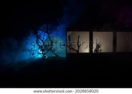 Artwork decoration. Old house with a big windows and zombies inside. Blurred scary silhouettes at window. Horror Halloween concept