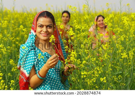 Indian rural villager woman farmer standing happily in a mustard field in a green farm yellow flowers enjoying the thriving agricultural crops in prosperity. Women standing in the background Royalty-Free Stock Photo #2028874874