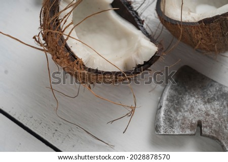 A coconut is chopped in half on a light wooden table. Top view