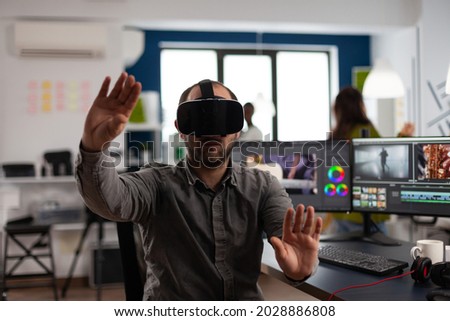 Designer creator wearing VR headphones gesturing while editing montage project in post production software sitting in studio office. Man videographer processing movie in digital multimedia company