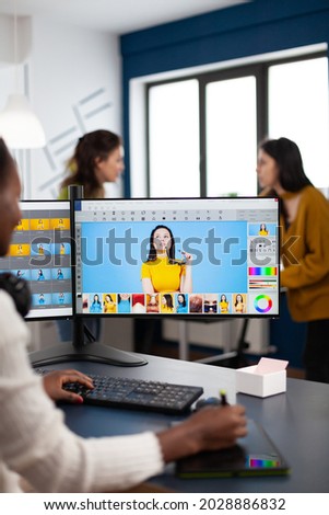 Black retoucher artist analysing images on pc with two monitors and retouching digital assets with stylus pencil. African designer using photo editing software working in creative production office