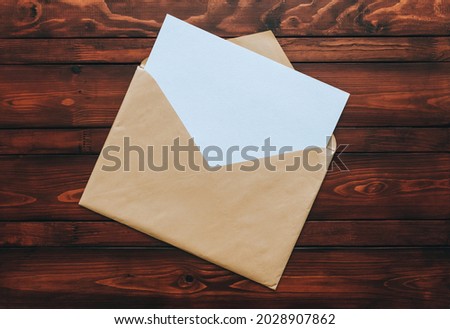 A large beige envelope of craft paper with a blank white sheet of paper inside lies on a brown wooden background. Blank letter concept with copy space.