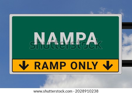 Nampa logo. Nampa lettering on a road sign. Signpost at entrance to Nampa, USA. Green pointer in American style. Road sign in the United States of America. Sky in background