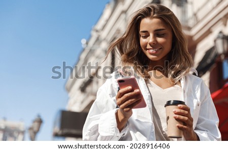 Beautiful smiling woman walking on street with coffee takeaway, chatting on mobile phone. Girl talking on smartphone on her way to meeting spot, sending message