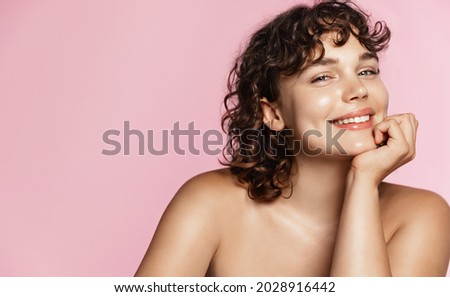 Teen model with curly hair and clean natural glowing skin, white smile, looking happy at camera. Promo of skin care and spa products for body and face. Pink studio background Royalty-Free Stock Photo #2028916442
