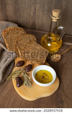 Herb-Infused Olive Oil. Olive oil with oregano and Kalamon or Kalamata olives and dried sprigs of rosemary with rye bread on the wooden board. 
