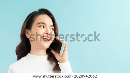 Portrait of a cute happy girl in dress talking on mobile phone and laughing isolated over blue background