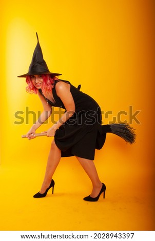 A woman on a yellow background on a broomstick on Halloween sits
