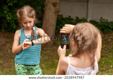 Two young little children, school age kids using electronic gadgets, kids and technology outdoors shot. Smart fit band and a smartphone, taking photos with a mobile phone concept, people, lifestyle