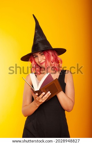 A magnificent witch girl in a black hat with a book of spells in her hands looks into the book and teaches at the school of magicians
