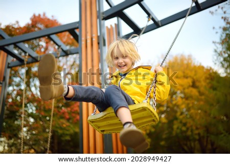 Little boy having fun on a swing on the playground in public park on autumn day. Happy child enjoy swinging. Active outdoors leisure for child in city Royalty-Free Stock Photo #2028949427