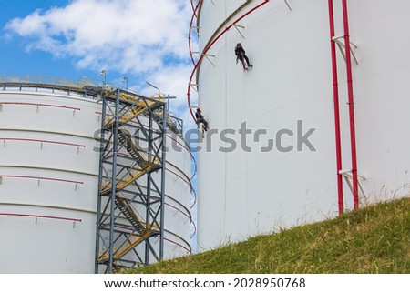Male two workers control rope down top roof tank rope access inspection of thickness shell plate storage tank gas safety work at height.