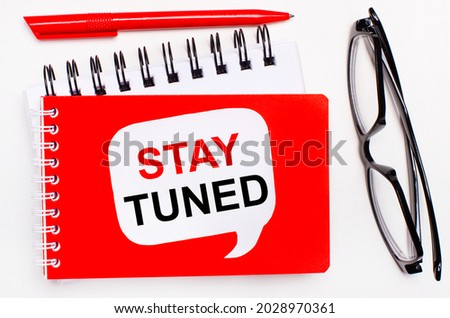 On a white background, white and red notepads, black glasses, a red pen and a white card with the text STAY TUNED.