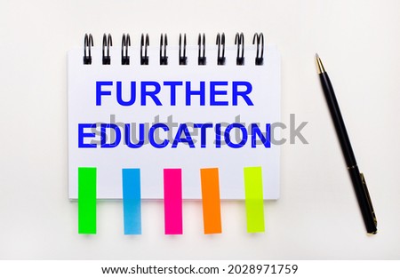 On a light background, a pen, a notebook with the text FURTHER EDUCATION and bright stickers.