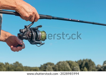 Male hands holding fishing rod or angler over blue clear sky in summer. Royalty-Free Stock Photo #2028985994
