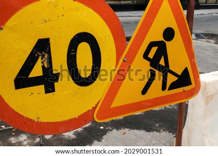 Traffic signs warn the existence of a construction site on a road. Dirty road signs block the road  in the city. Triangle Sign Road Works and Round Speed Limit Sign. Close-up