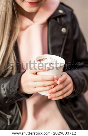 A beautiful teen girl in a black jacket and a pink bike holds a glass with hot chocolate or cocoa with marshmallows. Photo