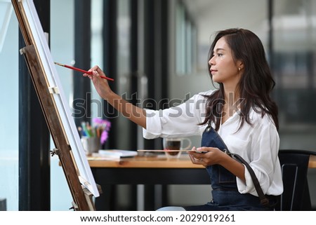 Young woman artist painting picture on canvas with water colors in her workshop.