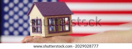 Small house with keys on hand against background of American flag