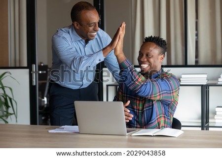 Smiling African American male colleagues give high five celebrate shared business victory or win. Happy ethnic men employees triumph for company success or good job results. Teamwork concept. Royalty-Free Stock Photo #2029043858