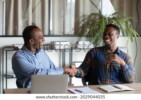 Overjoyed African American male business partners shake hands close deal after success office negotiation. Smiling biracial businessmen handshake get acquainted greet at meeting. Partnership concept.