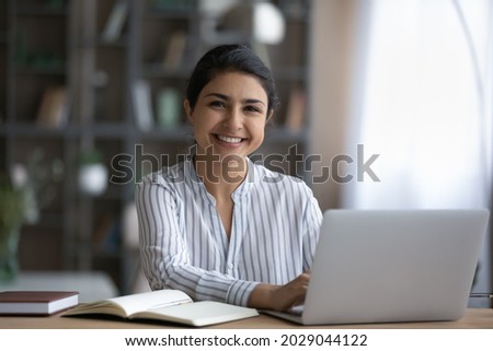 Portrait of happy millennial Indian female student sit at desk study distant on computer. Smiling young mixed race woman work online on modern laptop at home office. Technology, diversity concept. Royalty-Free Stock Photo #2029044122
