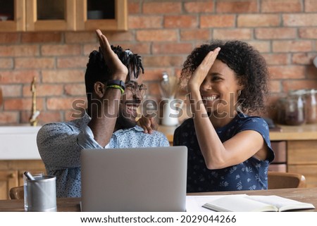 Happy excited Black mixed race couple celebrating financial success at laptop, getting income, loan, mortgage bank approval, planning good family budget. Young husband and wife giving high five Royalty-Free Stock Photo #2029044266
