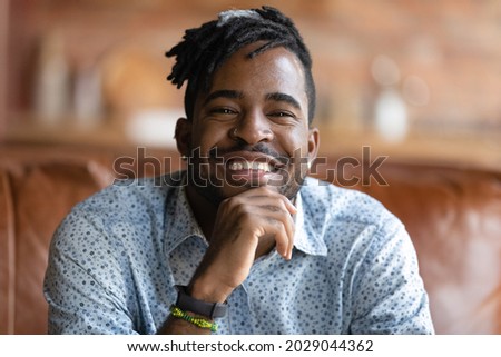Head shot portrait of happy millennial Black mixed race hipster guy looking and smiling at camera. Young stylish African man, coach, teacher giving training via video conference call. Screen view