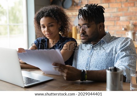 Serious millennial black married couple reading documents at laptop together, checking monthly bills, paying taxes, insurance, mortgage fees, planning family budget, doing domestic paperwork Royalty-Free Stock Photo #2029044401