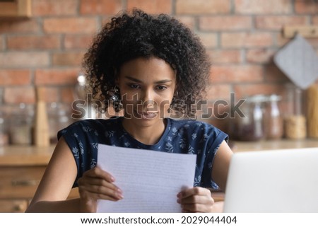 Focused Afro American student girl receiving important paper letter, acceptance notice from college, university, paid loan confirmation from bank, bill for insurance fee, tax payment. Paperwork Royalty-Free Stock Photo #2029044404