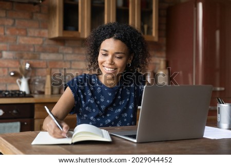 Happy smiling mixed race African student girl studying from home, writing notes, watching, listening, summarizing learning webinar on laptop, attending virtual school class, online college lesson Royalty-Free Stock Photo #2029044452