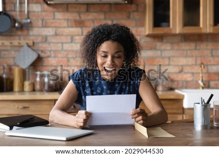 Happy millennial African American woman receiving good news from mail service, reading paper letter in home kitchen, smiling, shouting for joy. Student girl receiving acceptance notice from college Royalty-Free Stock Photo #2029044530
