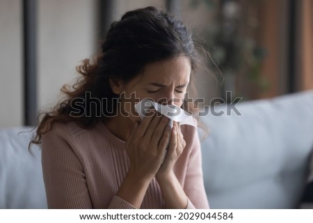 Sick young woman sit indoors holding tissue blowing running nose feels unhealthy looking unwell, having symptoms of sinusitis, chronic disease, suffers from seasonal allergy or cold fever, flu concept Royalty-Free Stock Photo #2029044584