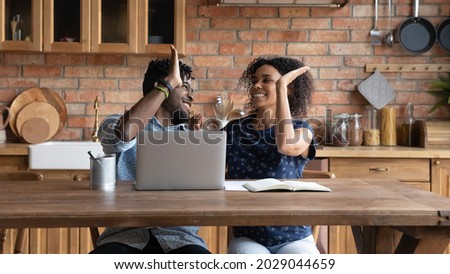 Happy successful Afro American couple celebrating financial achieve at laptop, giving high five. Married man and woman getting income, profit, loan, mortgage bank approval, feeling joy together Royalty-Free Stock Photo #2029044659