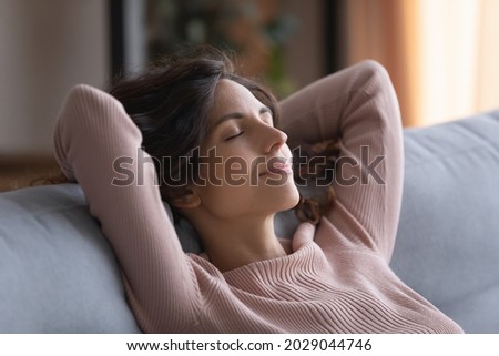 Smiling serene Hispanic woman close her eyes put hands behind head breath fresh conditioned air inside of modern living room, enjoy stress-free day off alone at home. Daydreams, peace of mind concept Royalty-Free Stock Photo #2029044746
