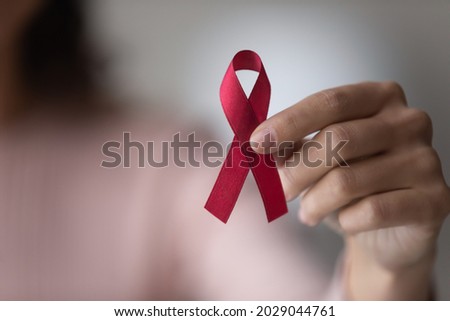 Close up focus on red ribbon in female hands, woman standing indoor promote annual regular health check up, support people with chronic disease, social AIDS campaign, HIV awareness, healthcare concept Royalty-Free Stock Photo #2029044761