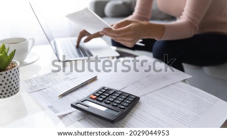 Accountant woman pay bills online use e-bank app, calculating household finances or taxes sit on sofa at home office. Family expenditures management, close up focus on calculator and heap of receipts Royalty-Free Stock Photo #2029044953