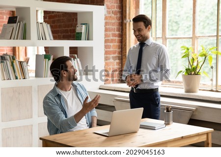 Male friends colleagues office employees talk enjoy pleasant conversation share business news gather at modern workplace. Good work relation, collaboration, mentor and apprentice communication concept