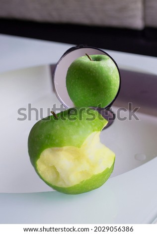 Bitten apple in the mirror is reflected complete. Concept of eating disorders such as anorexia or bulimia. Concept of social networks, shows a different life from the real one. Royalty-Free Stock Photo #2029056386