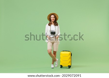 Full length fun traveler tourist woman in casual clothes straw hat hold yellow suitcase isolated on pastel green background. Passenger travel abroad on weekends getaway. Air flight journey concept.