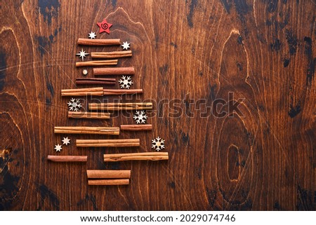 Christmas fir tree made from shaped cinnamon and anise spices with red and green Christmas balls on wood background for your xmas greetings. Top view with copy space.