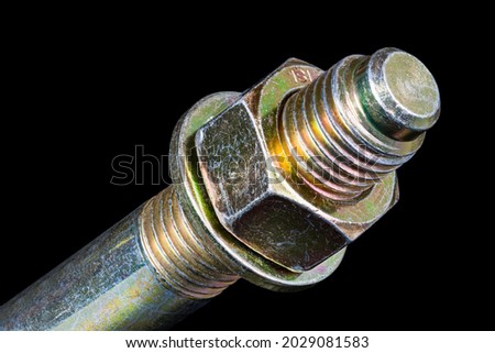 Hexagonal nut and washer on metal galvanized anchor bolt end on black background. Artistic detail of thread on anchoring rod into concrete with yellow chromate conversion coating to protect corrosion.