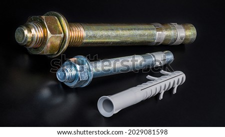 Galvanized wedge expansion anchor bolts and plastic split-ribbed dowel on a black background. Closeup of various fasteners for anchoring into concrete. Metal rods with thread, nuts and washers on end. Royalty-Free Stock Photo #2029081598