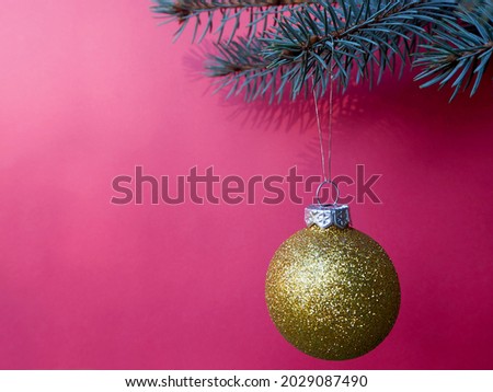 On the right, a round shiny golden Christmas toy hangs on a branch of a Christmas tree on a pink background. side view. copy space