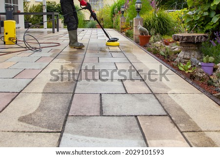 Cleaning stone slabs on patio with the high-pressure cleaner. Person worker in rubber boots cleaning the outdoors floor.  