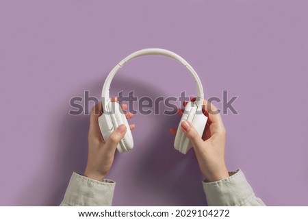 White headphones in humans hands flat lay on purple background. Audio sound, music gadgets minimalistic concept.