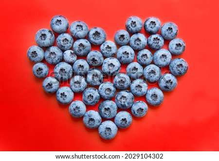 Heart made from fresh blueberries on a red background. Healthy eating concept.
