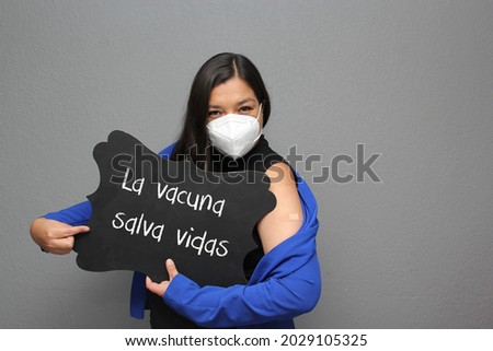 Latino adult woman shows her arm that just received the Covid-19 vaccine and a sign that says "The vaccine saves lives"
