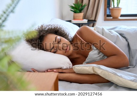 Young calm African American woman model sleeping well with eyes closed lying in comfortable bed on orthopedic mattress lying on soft pillow at home having healthy night sleep relaxing in the morning. Royalty-Free Stock Photo #2029127456